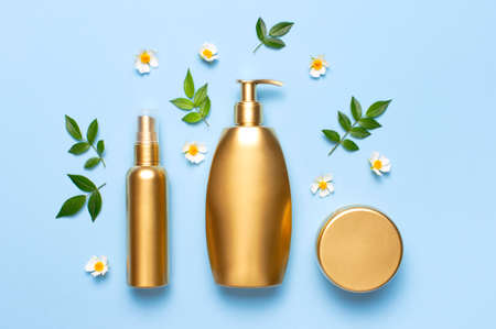 Cosmetic mock up gold bottles. Cosmetics, spring white flowers green leaves on blue background. Cosmetics Springtime Summer Concept. Flat lay top view copy space. Branding products, beauty background.の写真素材