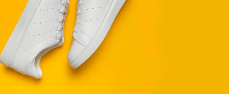 White women's leather sneakers on yellow background top view flat lay. Stylish youth sneakers, sports shoes, genuine leather footwear. Minimalistic shoe store advertising fashion style Shoe background.の写真素材
