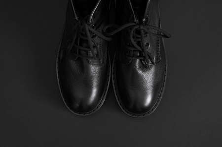 Fashionable youth black leather boots on black background flat lay top view. Stylish womens mens unisex boots. Grunge boots with bootlace. Clothes, shoes, fashion background. Classic leather shoes.の写真素材