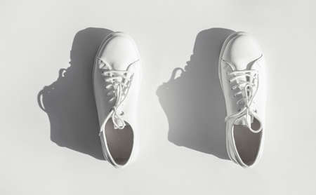 White women's leather sneakers with sun shadows on white background top view. Stylish youth sneakers, sports shoes, genuine leather footwear. Minimalistic shoe store advertising fashion style.の写真素材