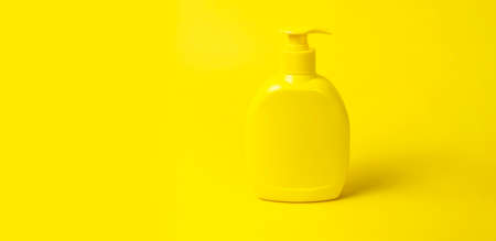 Yellow plastic cosmetic bottle container with dispenser on yellow background flat lay. Clean container without label for soap gel cream lotion shampoo bath foam. Beauty spa branding mockups.の写真素材