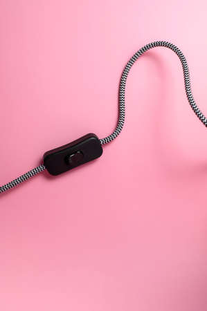 Wire with black switch from table lamp on pink background flat lay. Lighting, lamp, light, interior decor, electricity. Children's pink table lamp. Single piece of furniture. Metal designer lamp.の写真素材
