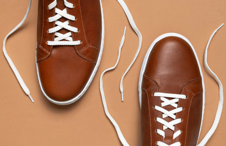 Leather brown men's sneakers with white laces and rubber soles on beige background. Flat lay top view. Men's sports casual shoes. fashionable sneakers. Male fashion hipster footwear Minimal background.の写真素材