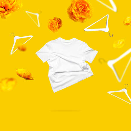 White flying cotton T-shirt white wooden hangers tulips on yellow background. Spring sale concept. Clean white t-shirt for women or men. Unisex Classic Basic T-shirt. Branding clothes Mock up.の写真素材