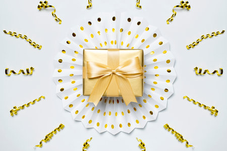 Festive concept. Carnival white and gold paper fans, gold gift with bow confetti on light background top view. origami. Decorative objects for party, birthday, holiday, wedding. abstract background.の写真素材