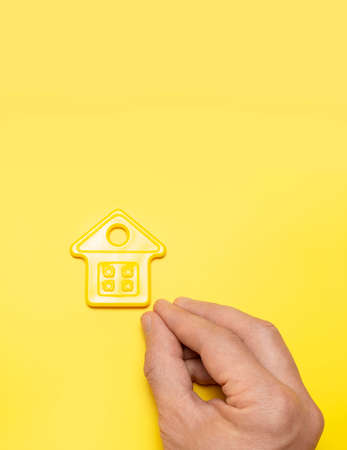 House symbol in male hands on yellow background flat lay top view. Model of plastic yellow house. Concept of buying home, apartment. Renting a house, real estate. Mortgage, real estate insurance.の写真素材