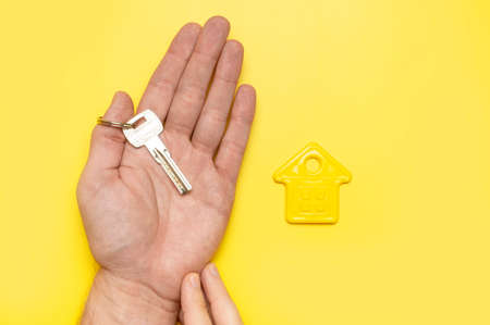 House symbol in male hands on yellow background flat lay top view. Model of plastic yellow house. Concept of buying home, apartment. Renting a house, real estate. Mortgage, real estate insurance.の写真素材