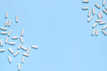 Pills, tablets, vitamins, food supplement in white capsules on blue background. Health concept, vitamin deficiency, avitaminosis, medical pharmaceutical background. Flat lay top view copy space.の写真素材