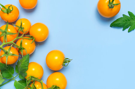Ripe fresh yellow orange tomatoes with green tails, leaves on blue background flat lay top view....