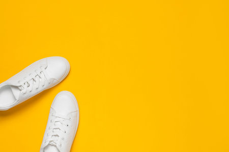 White women's leather sneakers on yellow background top view flat lay. Stylish youth sneakers,...
