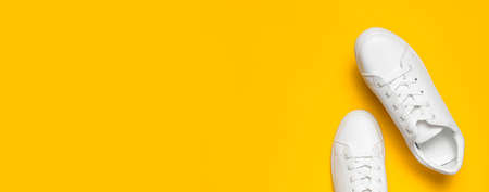 White women's leather sneakers on yellow background top view flat lay. Stylish youth sneakers, sports shoes, genuine leather footwear. Minimalistic shoe store advertising fashion style Shoe background.の写真素材
