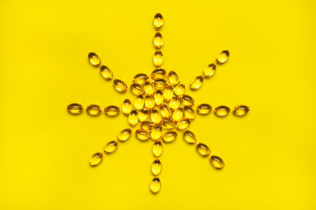 Capsules pill vitamin D sun shaped on yellow background close-up. Fish oil, Omega, Omega-3, dietary...