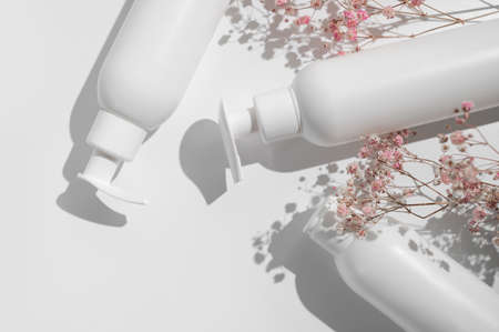 White clean cosmetic bottles, pink dry twigs of flowers on white background flat lay top view. Plastic packaging cosmetic products for branding and label, mock up. Spa, Shampoo, lotion, moisturizer.の写真素材