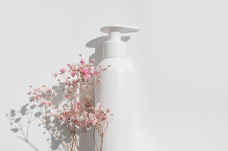 White clean cosmetic bottles, pink dry twigs of flowers on white background flat lay top view. Plastic packaging cosmetic products for branding and label, mock up. Spa, Shampoo, lotion, moisturizer.の写真素材