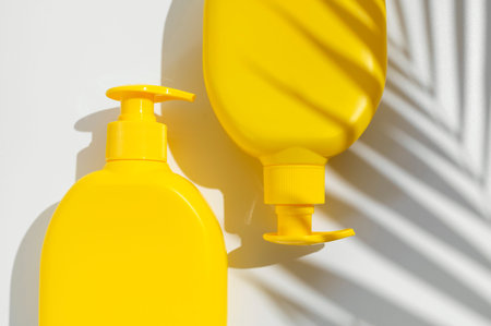 Yellow cosmetic bottle, tropical leaf shadow on white background flat lay top view. Plastic packaging cosmetic products for branding and label, mock up. Spa, Shampoo, lotion, moisturizer soap, mock up.の写真素材