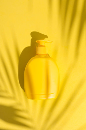 Yellow plastic cosmetic bottle, tropical leaf shadow on yellow background flat lay top view. Plastic...