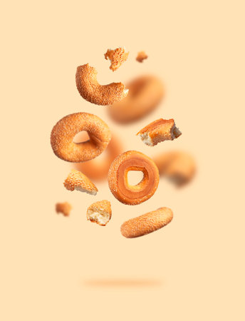 Creative food, baking layout. Fresh round wheat bagel with sesame seeds flying on beige background. Crispy bread, healthy organic food, traditional pastries, bakery product. Breakfast bagel.の写真素材