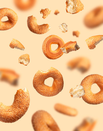 Creative food, baking layout. Fresh round wheat bagel with sesame seeds flying on beige background. Crispy bread, healthy organic food, traditional pastries, bakery product. Breakfast bagel.の写真素材