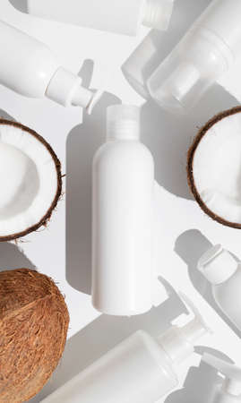 White cosmetic bottles, broken fresh coconut with sunny contrast shadows on light gray background top view. Organic natural cosmetics with coconut oil. Plastic packaging products for branding, mock up.の写真素材