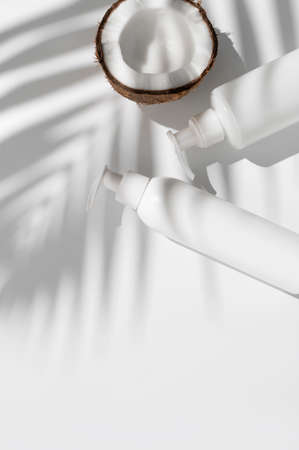 White cosmetic bottles broken fresh coconut with sunny contrast shadows palm leaf on gray background. Organic natural cosmetics with coconut oil. Plastic packaging products for branding, mock up.の写真素材
