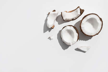 Fresh whole and broken pieces tropical coconut nut with sunny contrast shadows on light gray background flat lay top view. Creative summer food background, exotic organic healthy diet fruit.の写真素材