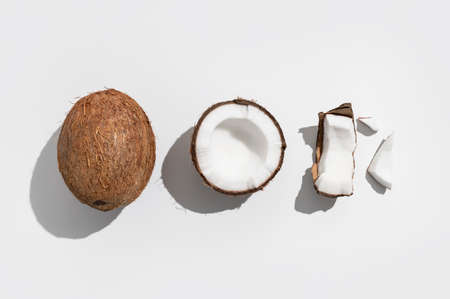 Fresh whole and broken pieces tropical coconut nut with sunny contrast shadows on light gray background flat lay top view. Creative summer food background, exotic organic healthy diet fruit.の写真素材