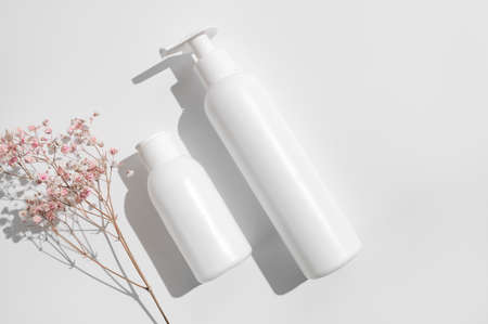 White clean cosmetic bottles, pink dry twigs of flowers on white background flat lay top view. Plastic packaging cosmetic products for branding and label, mock up. Spa, Shampoo, lotion, moisturizer.の写真素材