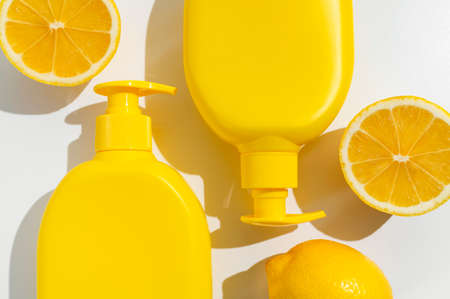 Yellow plastic cosmetic bottles, fresh whole lemon and halves on white background flat lay top view. Organic natural cosmetics with lemon extract. Moisturizing soap, cream, body lotion, sunscreen.の写真素材