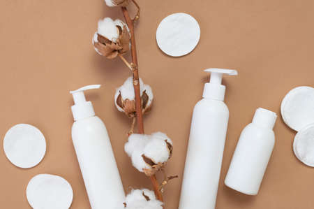 Cosmetics SPA branding mock-up. White cosmetic bottle containers, branch of cotton, cotton pads, ear sticks for hygiene on brown background top view flat lay. Natural organic beauty product concept.の写真素材