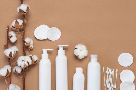 Cosmetics SPA branding mock-up. White cosmetic bottle containers, branch of cotton, cotton pads, ear sticks for hygiene on brown background top view flat lay. Natural organic beauty product concept.の写真素材