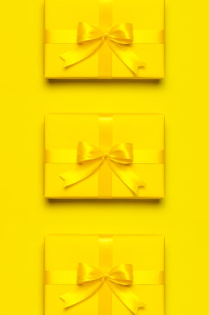 holiday pattern. Yellow gift box with ribbon and bow on bright yellow background flat lay top view....