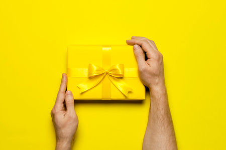 holiday concept. Male hands holding yellow gift box with bow on yellow background flat lay top view. Surprise, gift for birthday, mother's day, March 8, Christmas, anniversary. Congratulations.の写真素材