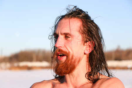Young Good Looking And Attractive Man With Muscular Body, with a red beard and long hair Wet Taking after taking an ice bath. handsome attractive men showering next to swimming pool. water drops are falling on his torso. Sunny winter day in Ukraine, Shostkaの写真素材