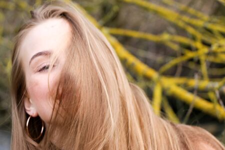Pretty young woman posing at camera outdoor. Bulrush background. Outdoor. Close up. On a sunny day near the dry reed and blue lake. Beautiful blonde with long hair In a brown coatの写真素材