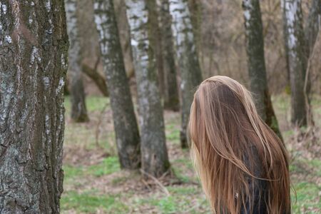beautiful girl, blonde with long hair, walks in the spring near the forest in a long blue dress and a black jacket, serenity and freedomの写真素材