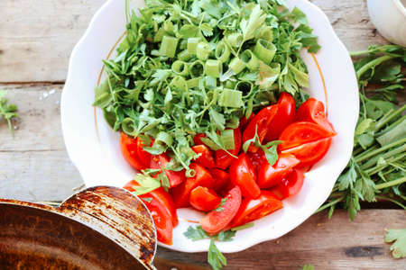 Fresh ingredients of salad on cutting board. Top view organic vegetables red tomatoes, cucumbers, bunch of parsley and green onion. Dieting food, vegetarian menu concept.の写真素材