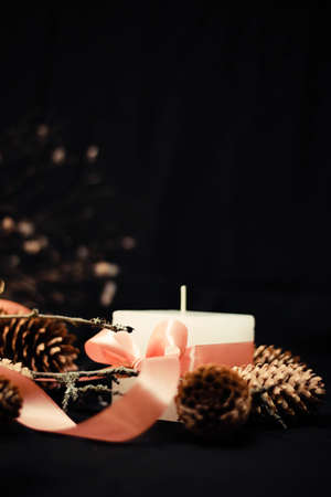 Pink Christmas decorations with candlelight, pink ribbons, twigs, dry grass, including sparkling baubles, ribbons and pine cones, on a black background.の写真素材