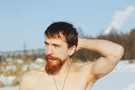 young, slim, handsome, sporty man with a red beard and long hair, naked, diving after a swim in icy water, on a sunny frosty day into ice-cold water in winter, against the backdrop Ukraine, Shostkaの写真素材
