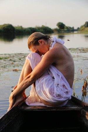 portrait of a beautiful young woman, with freckles and green eyes. a beautiful sunset light. athletic body, in a boat, against the background of waterの写真素材