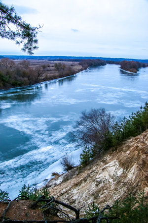 Frozen river covered with snow and ice, top view. Sandy hill with pine trees. Winter forest and river, snowy nature. Winter frosty day. beautiful ice textureの写真素材