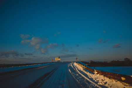 beautiful landscape winter white road among trees, blue sky with clouds sunny day, all in snow, warm sunset lightの写真素材