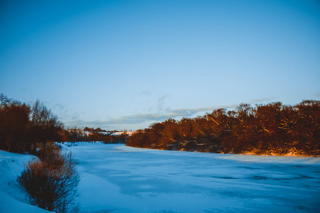 Winter forest on the river at sunset. Colorful landscape with snowy trees, beautiful frozen river with reflection in water. Seasonal. Winter trees, lake and blue sky. Frosty snowy river. Weatherの写真素材