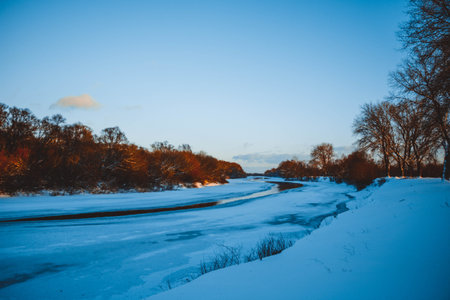 Winter forest on the river at sunset. Colorful landscape with snowy trees, beautiful frozen river with reflection in water. Seasonal. Winter trees, lake and blue sky. Frosty snowy river. Weatherの写真素材