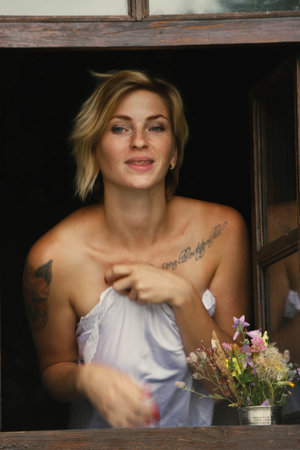 Art portrait of a beautiful young woman, looks through an old window peeps out, sits on the...