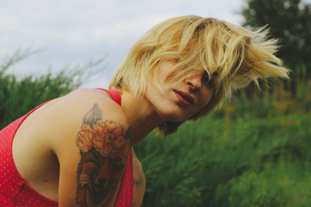 Young adult beautiful happy attractive European blonde woman portrait, have fun enjoy on green garden outdoor background. Female man in red clothes vintage retro pin up styleの写真素材