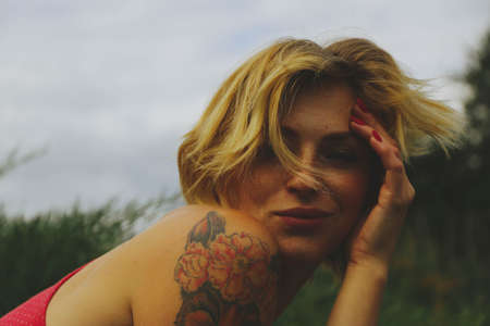 Young adult beautiful happy attractive European blonde woman portrait, have fun enjoy on green garden outdoor background. Female man in red clothes vintage retro pin up styleの写真素材