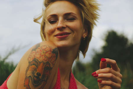 Young adult beautiful happy attractive European blonde woman portrait, have fun enjoy on green garden outdoor background. Female man in red clothes vintage retro pin up styleの写真素材