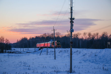 an old passenger train arrives at the station on a cold winter evening at sunset. Snowy landscape,...