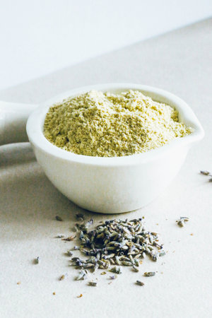 Ubtan powder with oatmeal in a container for gentle face cleansing on light background. Organic skin...