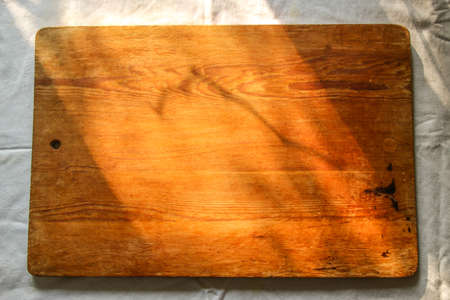 old wooden board on a white linen tablecloth and lace towel sunny natural light, shade. kitchen table top view. Beautiful retro, rustic background, free space.の写真素材